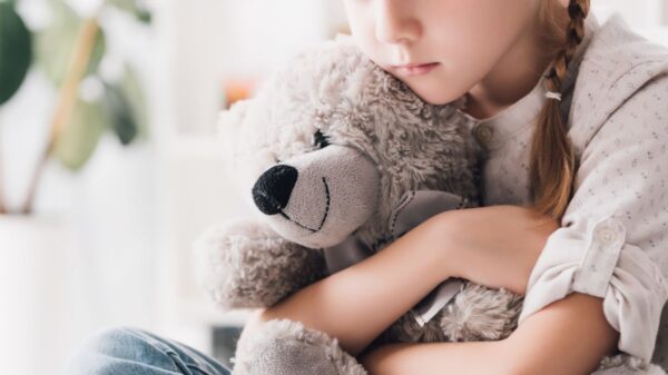 cropped shot of depressed little child embracing her teddy bear